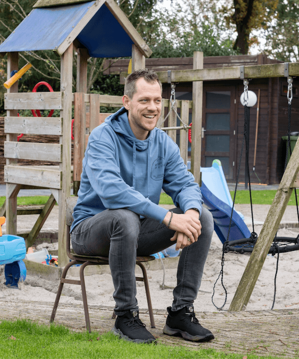 Wesley Kreder zit ontspannen op een stoel bij een speeltuin en lacht